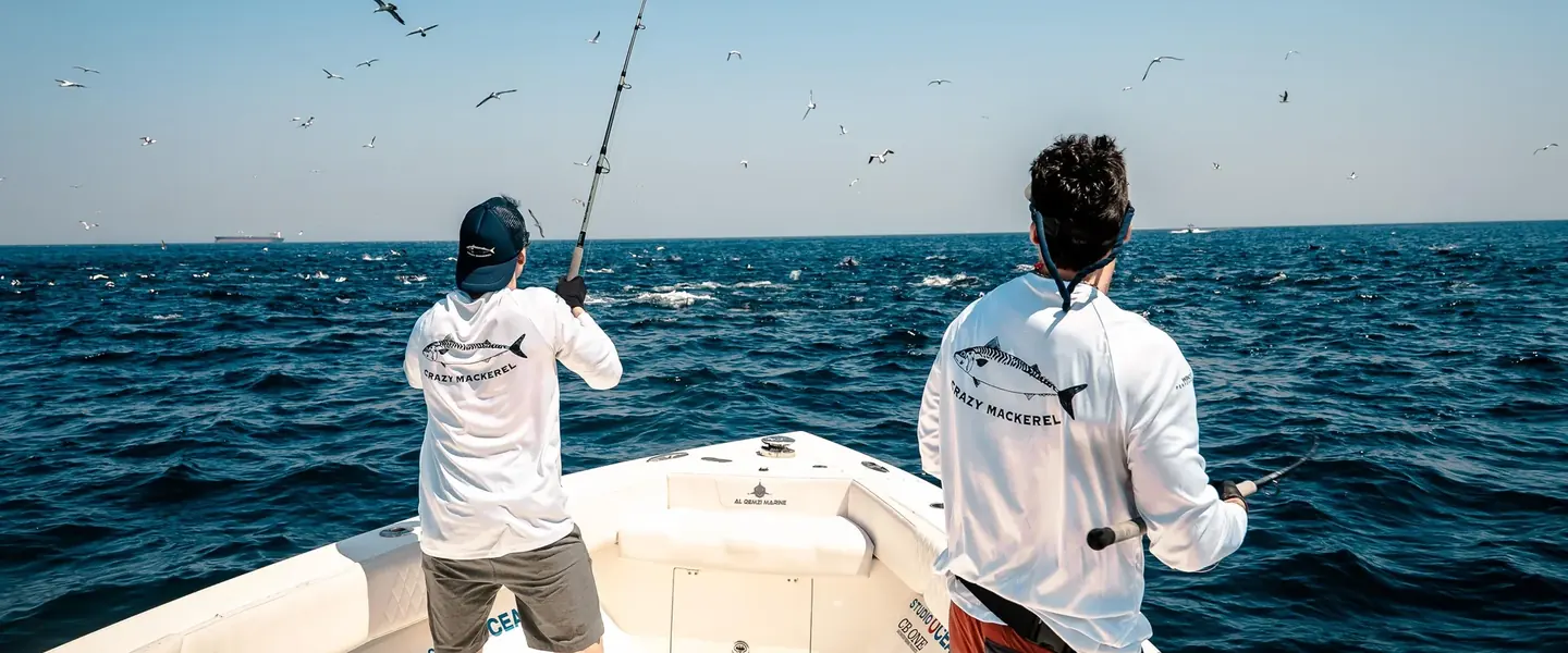 Deux pêcheurs en mer portant des tee-shirts manches longues Crazy Mackerel, vus de dos sur un bateau